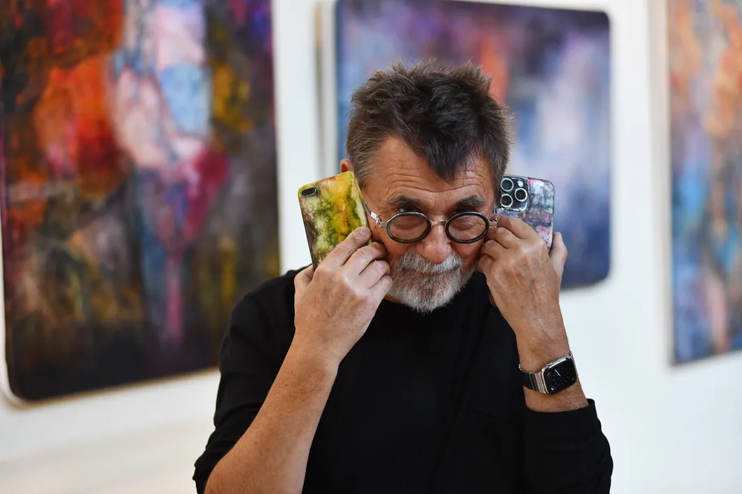Andrzej Walczak z malowanymi telefonami na tle swoich obrazów, Chełm, 2024